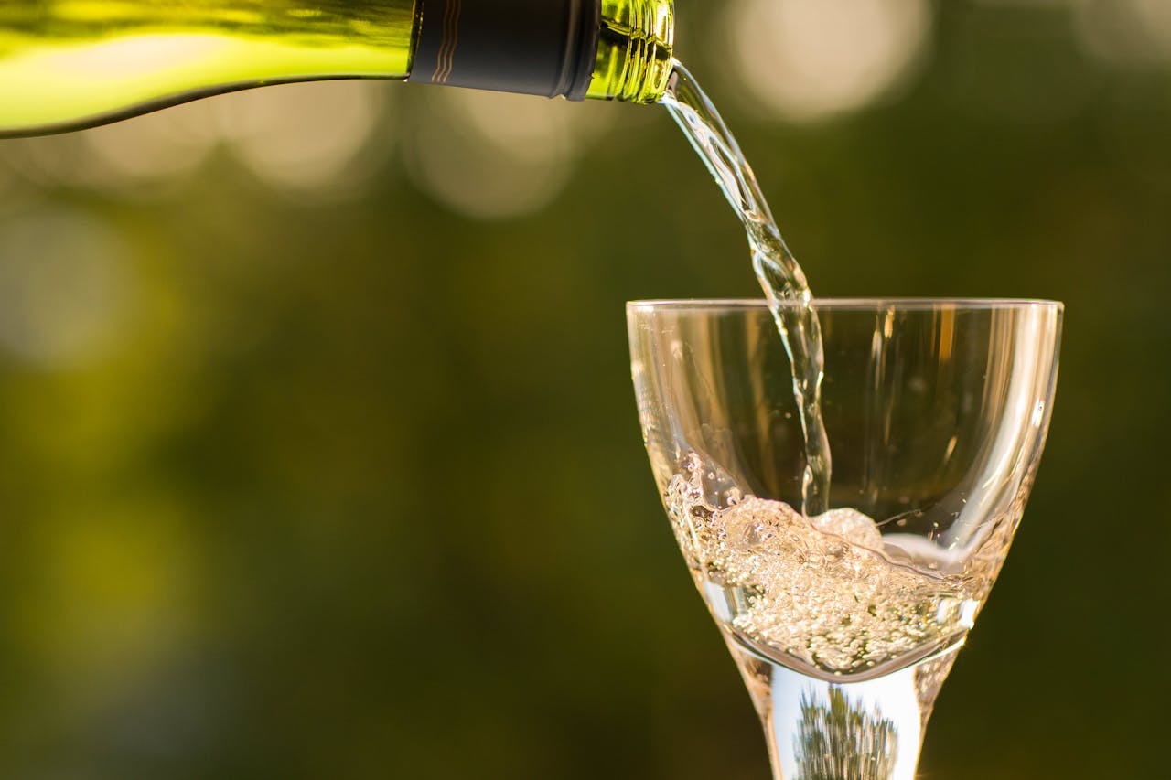about-02 Close-up of wine being poured into a glass with a green bokeh background.